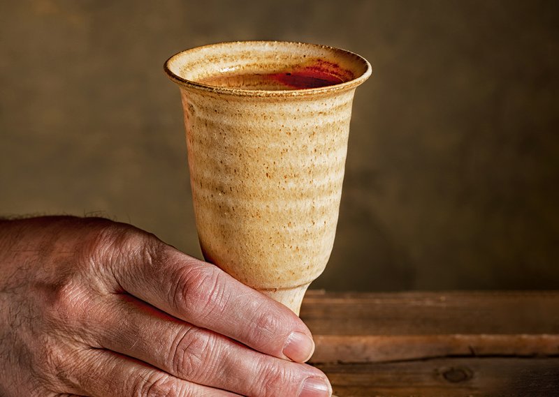 Tonkelch, der mit Wein gefüllt ist, eine Hand taucht gerade ein Brotstück ein.